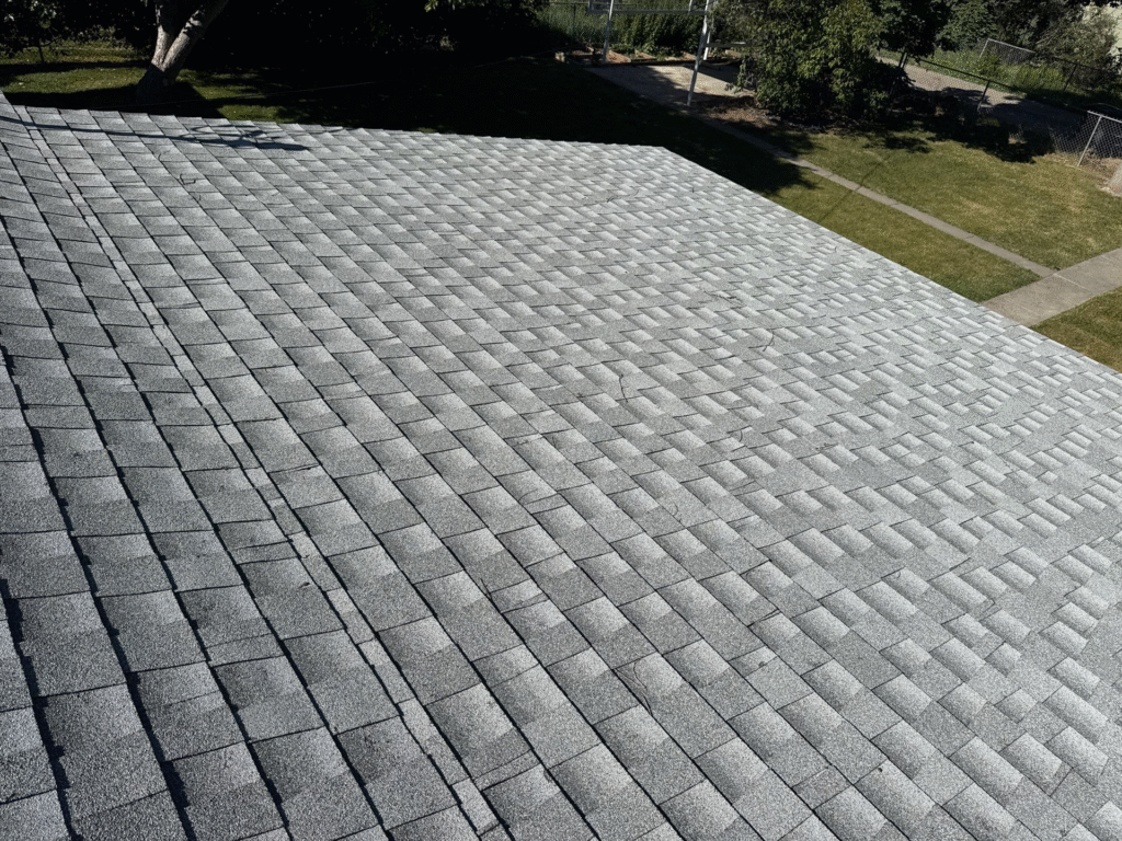 Close-up aerial view of a residential roof covered with traditional gray asphalt architectural shingles, showing slight signs of wear, potentially needing Billings Hail Proof Roofing replacement by Wegner Roofing & Solar.