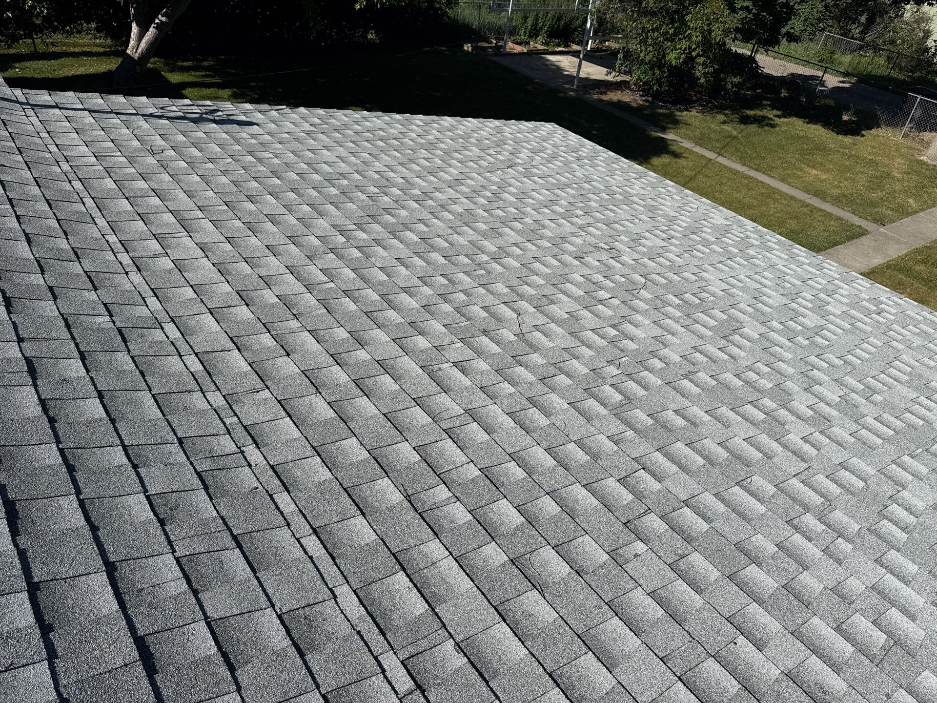 Close-up aerial view of a residential roof covered with traditional gray asphalt architectural shingles, showing slight signs of wear, potentially needing Billings Hail Proof Roofing replacement by Wegner Roofing & Solar.