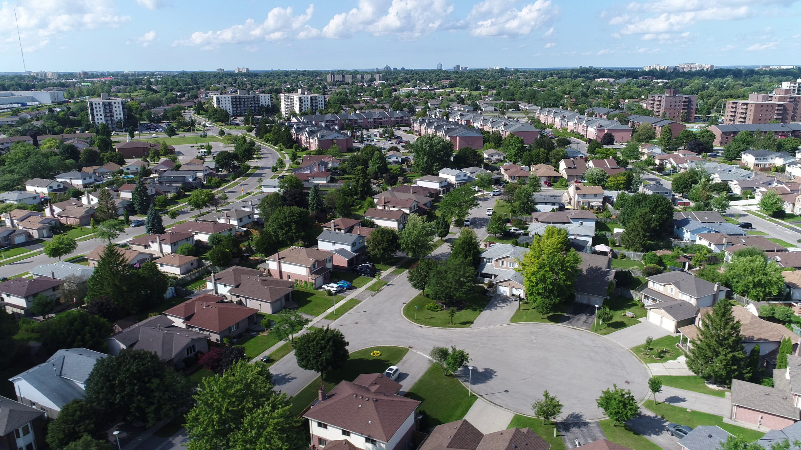 Aerial view of an established suburban neighborhood featuring single-family homes and mature trees along winding streets and a cul-de-sac, with taller apartment or commercial buildings in the background, representing Billings Mt Real Estate by Living in Billings.