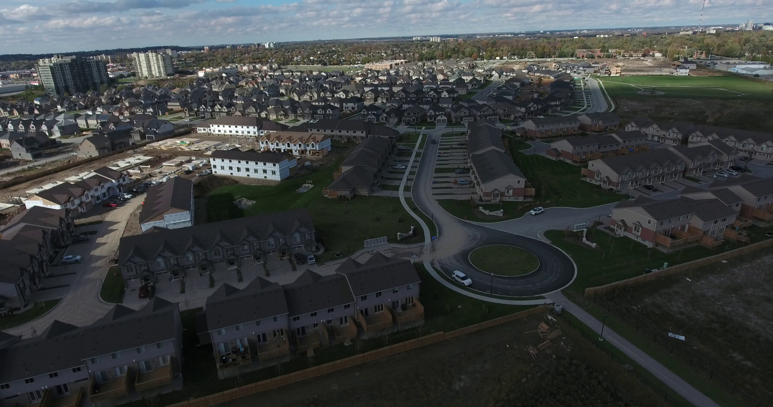 Aerial view of a newly developed residential area with numerous modern attached townhouses and single-family homes, featuring new roads, a roundabout, and areas of ongoing construction, showcasing new Billings Mt Real Estate developments by Living in Billings.