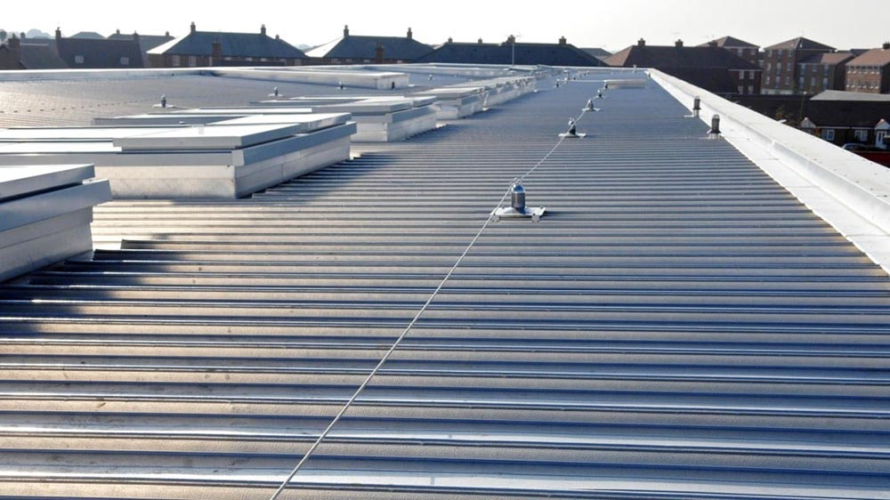 Wide view of a large, commercial style Bismarck Metal Roofing installation featuring a safety line system. The light gray corrugated metal roof demonstrates the durable work of Wegner Roofing & Solar.