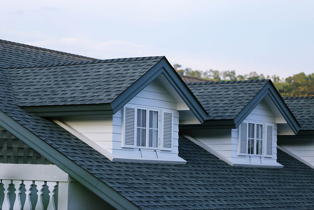 A close-up of a perfectly installed dark shingle roof with two white dormer windows, highlighting the detailed craftsmanship of the Columbia SC Residential Roofing Services by Burish Builder Columbia.