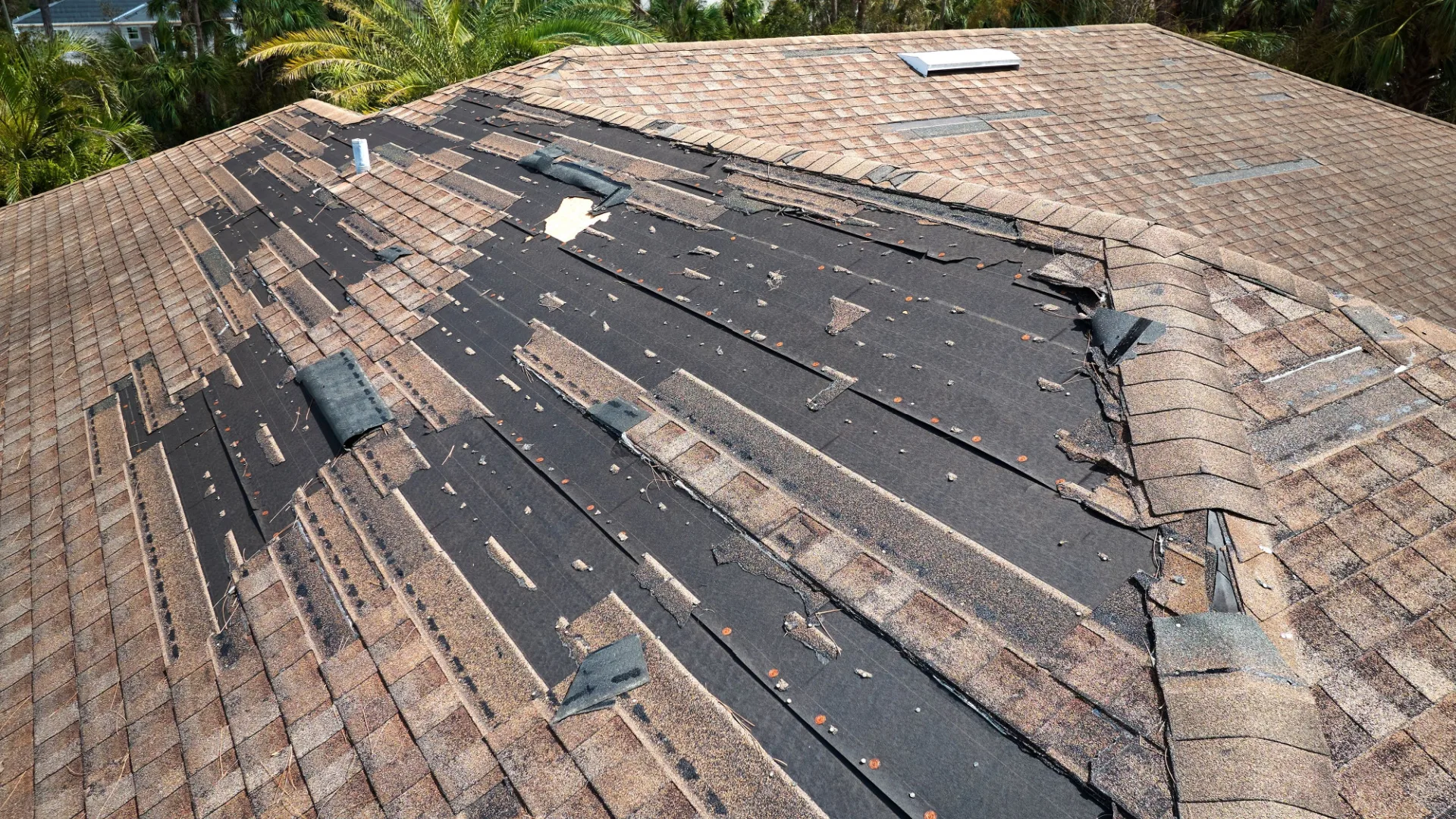 An aerial view of a damaged residential roof, showing missing and torn asphalt shingles, exposing the underlying dark roofing felt. This illustrates the need for Edmond OK Residential Roof Repair by Roof One.