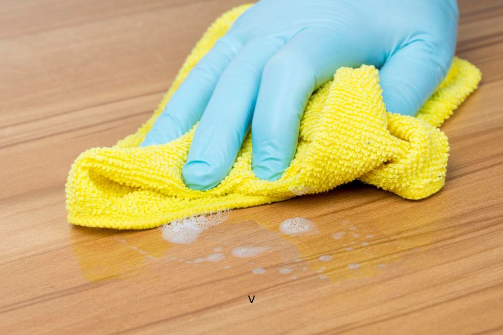 Professional cleaning hardwood surface with yellow cloth during Greensboro hardwood wax removal process.