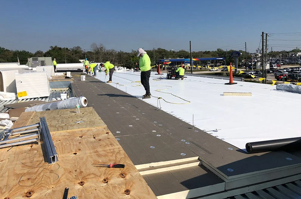 A crew of workers in bright safety vests installing white commercial roofing material (TPO/PVC) on a flat roof, demonstrating commercial services by Hendersonville TN Roofing Company by Burish Builder TN.