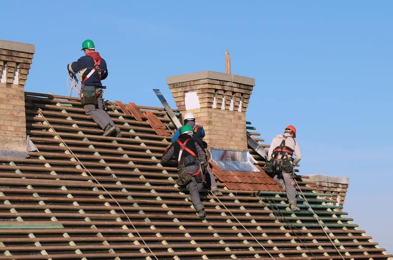 Two roofers installing corrugated red roofing material, part of a "Hendersonville TN Roofing Replacement" project by Burish Builder TN.
