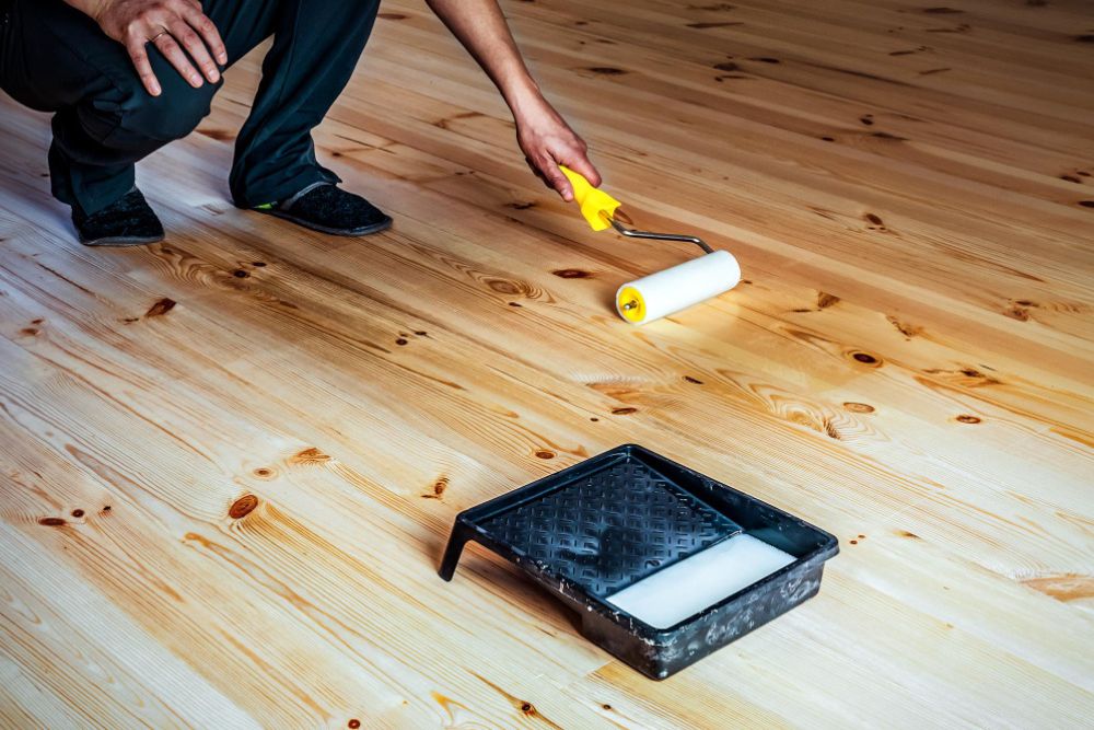 Professional applying finish on hardwood floor using roller during High Point hardwood floor refinishing project