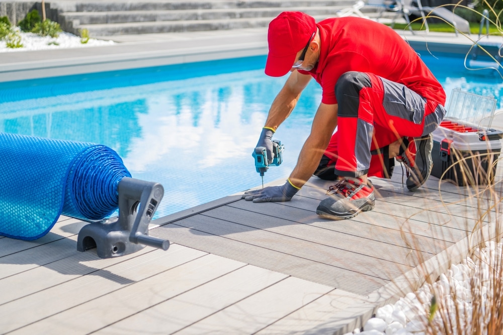 Pool installer in red working on the decking near a swimming pool, showing services by Mooresville Swimming Pool Installers by Craft Master Pools and Spas.