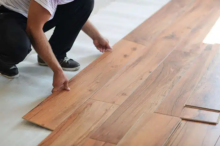 Newton NC Hardwood Floor Installation by Good House Floor Care: A contractor is shown laying a plank of rich brown hardwood flooring.