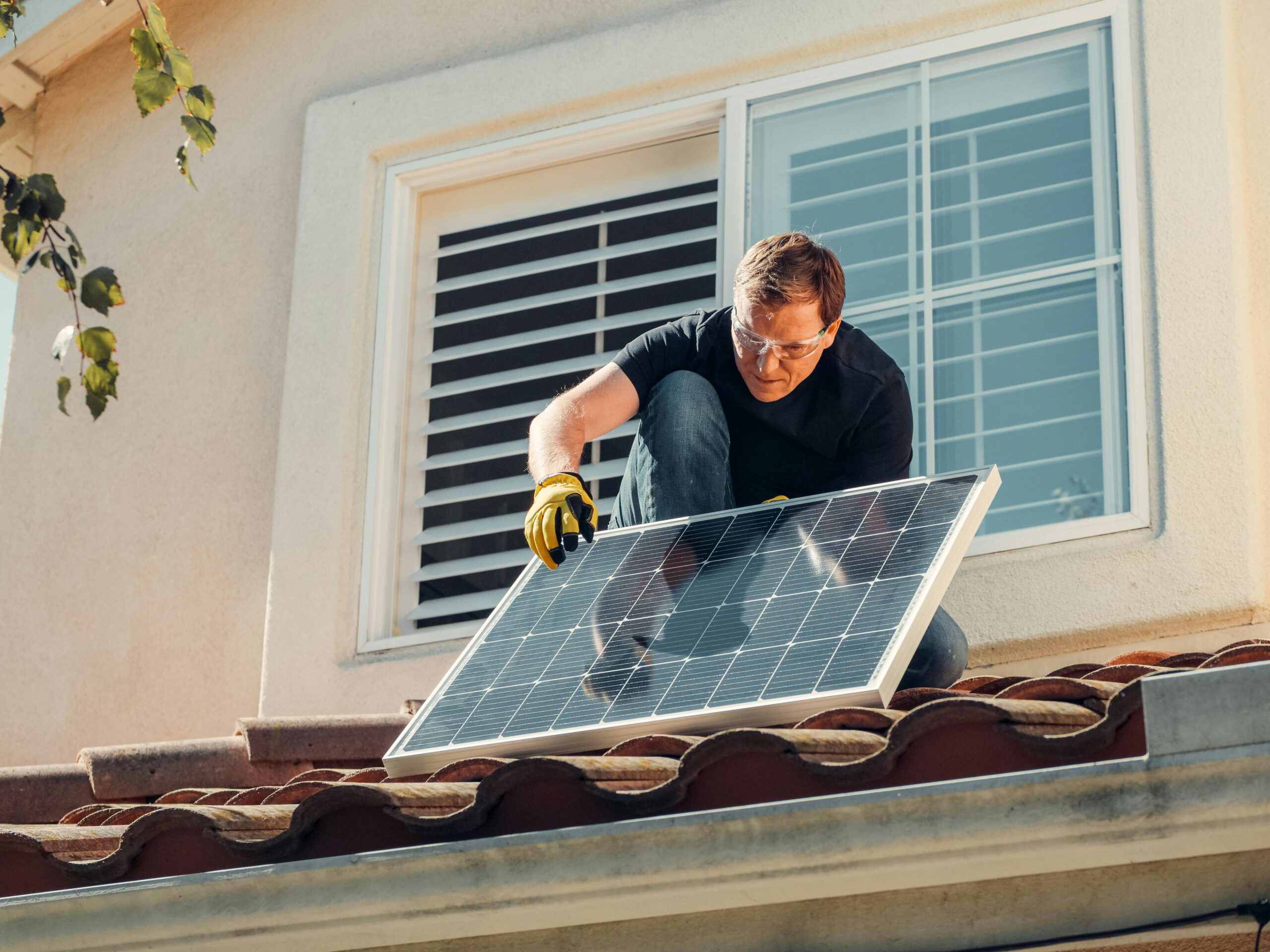 Palm Springs Solar Roofing Contractors by FL Pro Roofing & Solar: An installer wearing safety glasses and gloves kneels on a Spanish tile roof, positioning a solar panel.