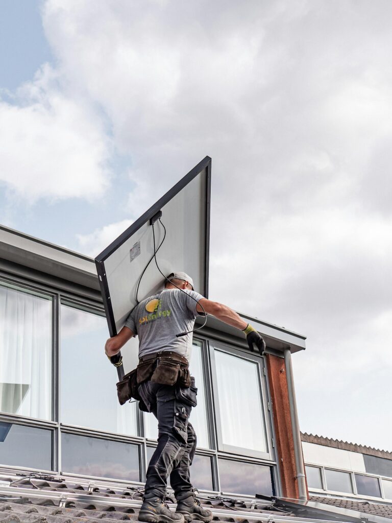 Palm Springs Solar Roofing Contractors by FL Pro Roofing & Solar: A contractor, with the company logo visible on his shirt, carries a large solar panel up onto a commercial roof.