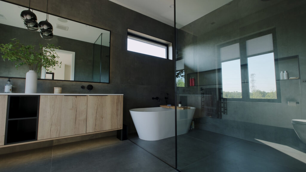 A sleek, modern bathroom with a dark gray tiled shower and floor, a contemporary white freestanding bathtub, and a light wood vanity with a white countertop, demonstrating a stylish and functional Aurora IL Shower Remodelling by Dream Bath Solutions.