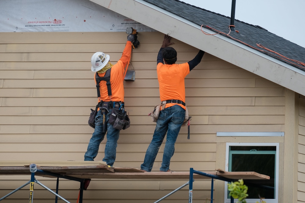 Two Bozeman Siding Contractors from Wegner Roofing & Solar working high on scaffolding to install siding near the peak of a residential roof.
