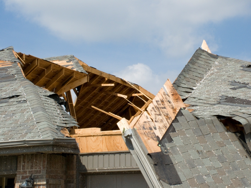Catastrophic structural roof damage on a house, with a large section of the roof blown away to expose the wood framing underneath, clearly showing significant Carver MN Storm Damage Repair needed from a service like Pro24 Contracting, Inc.