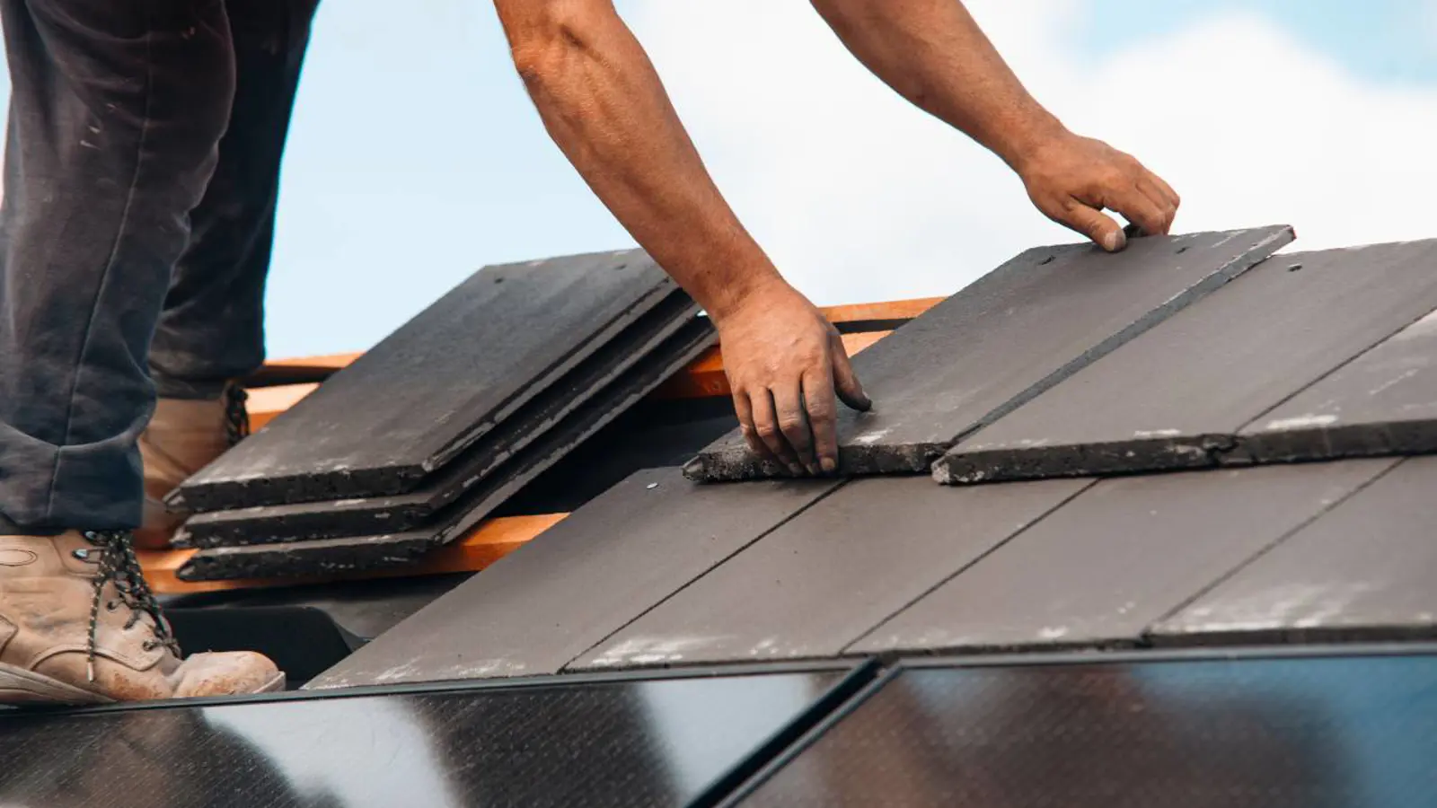 Close-up of a roofer installing dark slate or composite tiles on a roof, part of a Concord NC Roofing Replacement project by Burish Builder CLT.