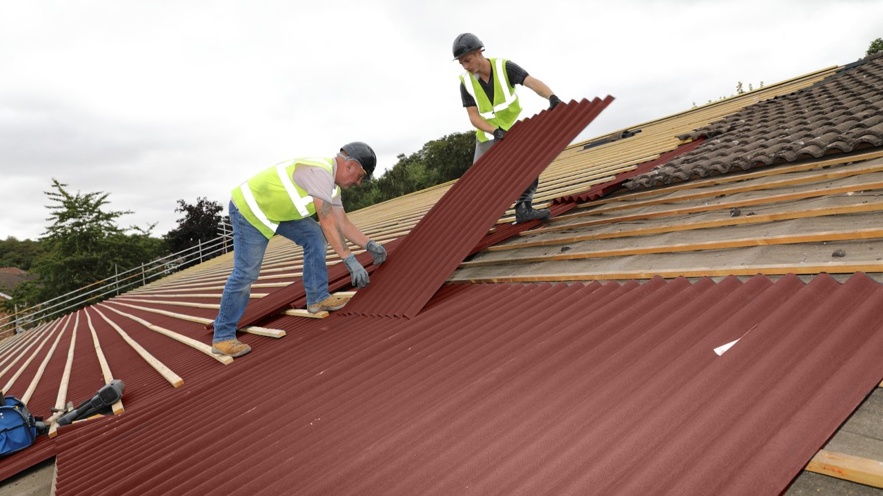 Two roofers in safety vests and helmets installing large sections of red corrugated roofing material, illustrating a Concord NC Roofing Replacement in progress by Burish Builder CLT.