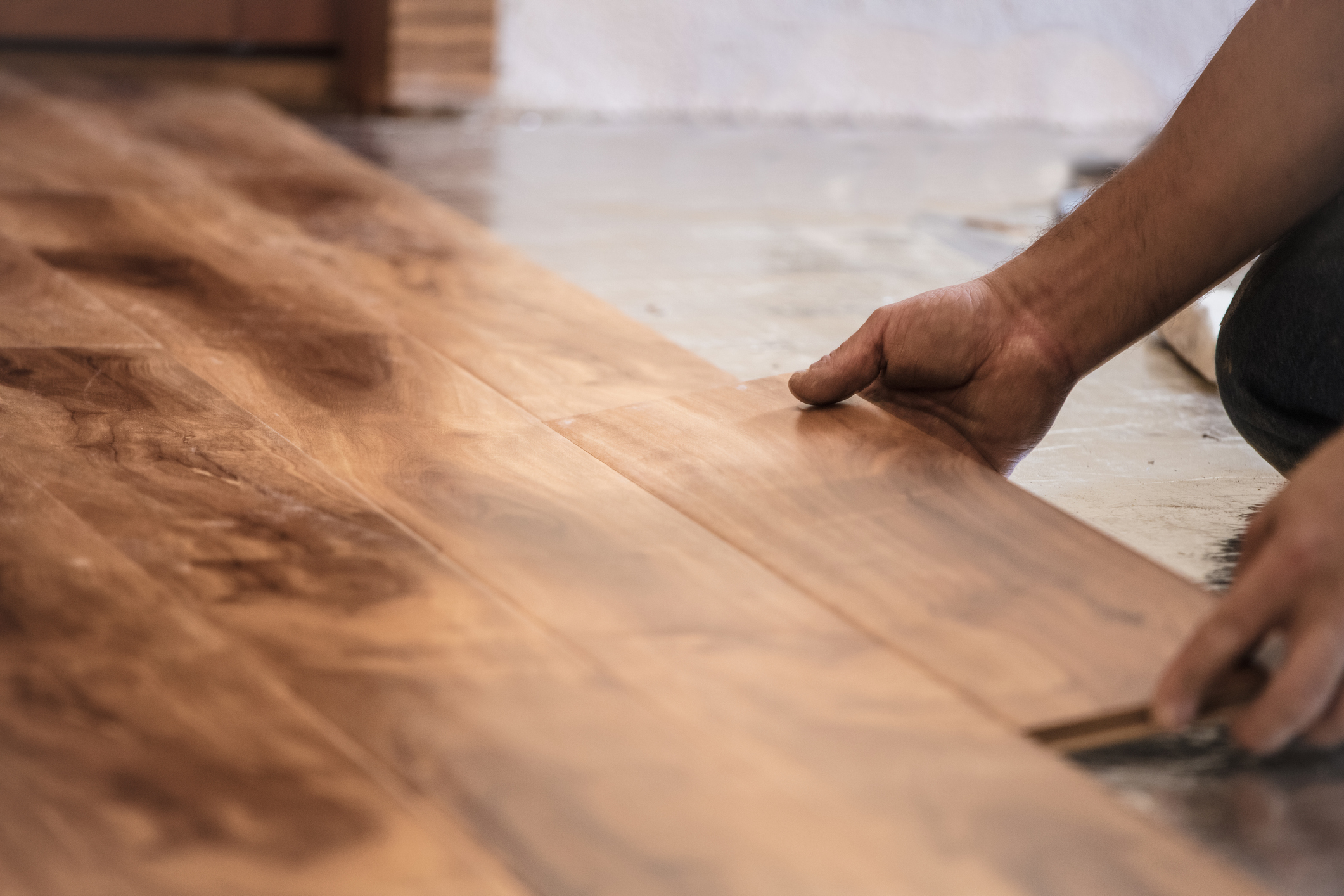 A close-up shot shows a worker from Peachy Flooring Solutions installing hardwood flooring in Roswell, GA, carefully placing a wooden plank into position, highlighting the ongoing hardwood floor installation Roswell GA.