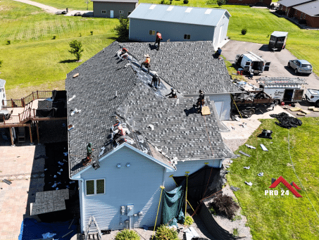 Ramsey MN Storm Damage Repair by Pro24 Contracting, Inc.: Overhead view of a residential roof in progress, showing multiple workers applying new gray shingles after storm damage removal.