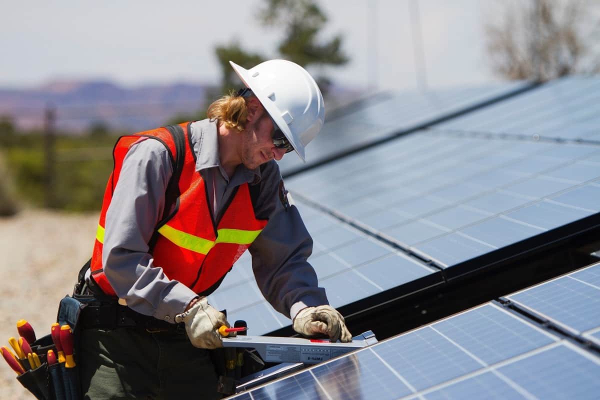 A Rapid City Solar Installation Companies professional from Wegner Roofing & Solar, wearing a hard hat and safety vest, adjusts a solar panel on a rooftop installation.