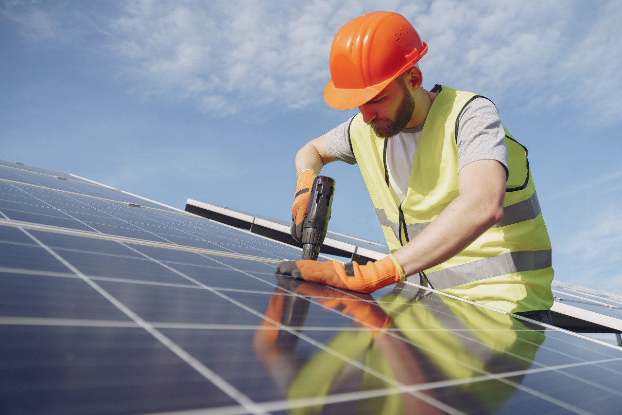 A Rapid City Solar Installation Contractor by Wegner Roofing & Solar wearing an orange hard hat and safety vest, installing a solar panel on a roof with a power drill.