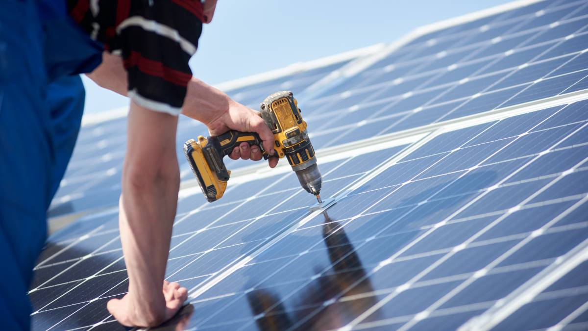 Close-up of an installer's hand using a yellow cordless drill to fasten a solar panel to a mounting bracket, showing the detail of a Rapid City Solar Installation Near Me project by Wegner Roofing & Solar.
