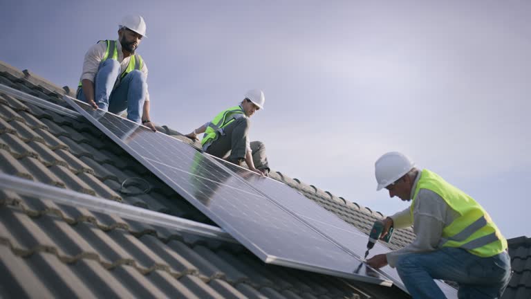 Rapid City Solar Installer team from Wegner Roofing & Solar installing solar panels on a tiled residential roof. Three workers in hard hats and high-visibility vests are carefully placing and securing the photovoltaic panels.