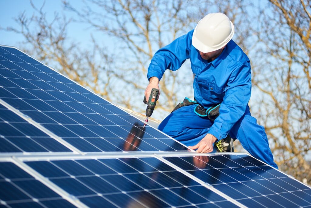 Close-up of a technician in a blue uniform and white hard hat using a power drill to secure a solar panel, showcasing the expert Rapid City Solar Panel Installation services available from Wegner Roofing & Solar.