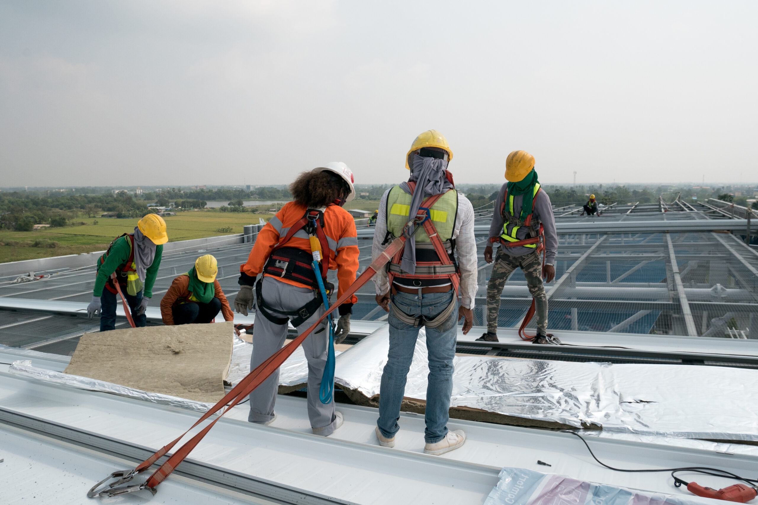A team of Spearfish Commercial Roofers by Wegner Roofing & Solar working on the large, flat roof of a commercial structure, demonstrating safe work practices while installing roofing materials, with a wide, open landscape in the background.