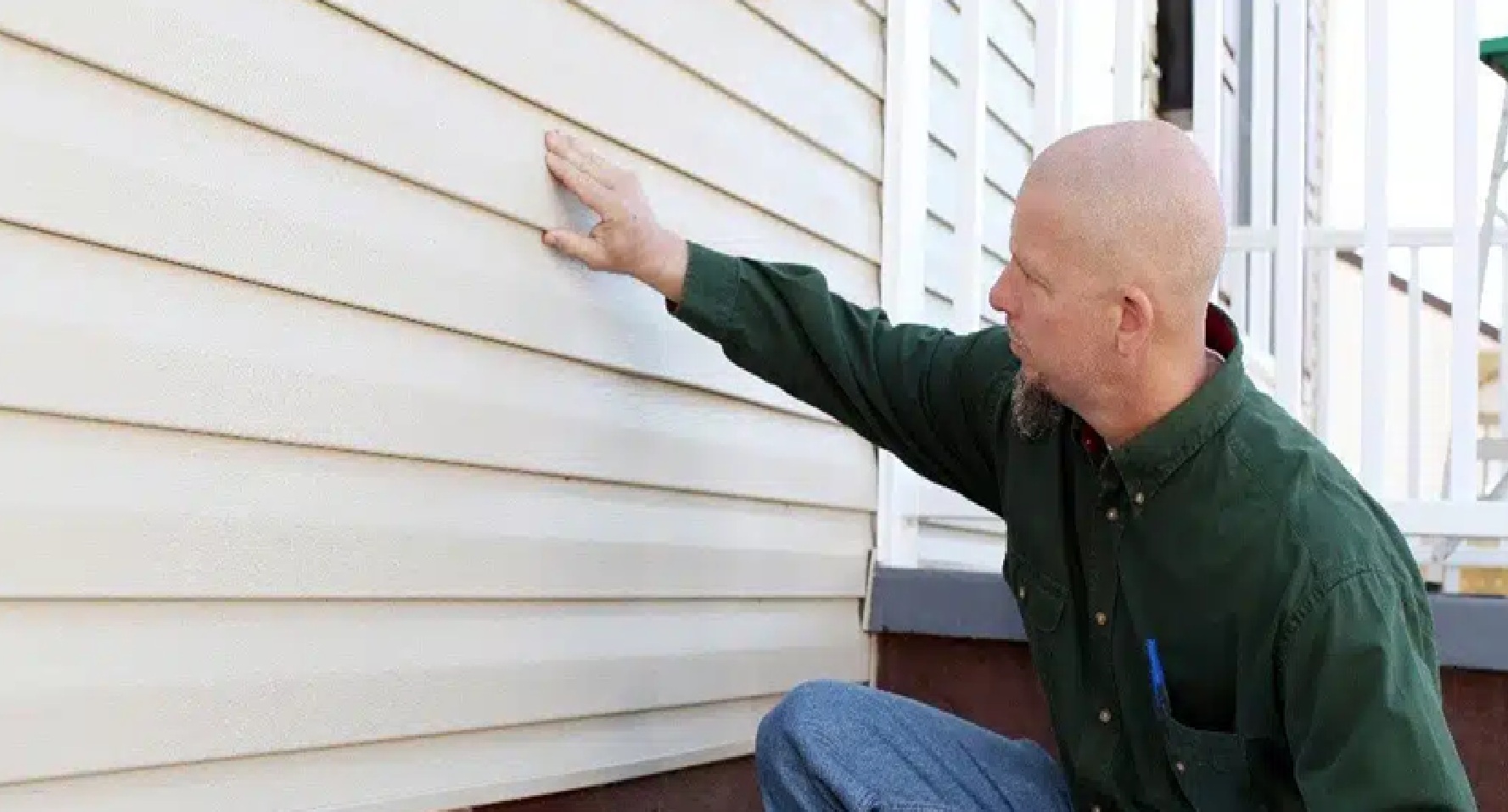 A worker from Wegner Roofing & Solar kneels down, running his hand over a section of horizontal beige siding to check for quality and seamless installation. This depicts the hands-on inspection provided by the trusted Spearfish Siding Contractors.