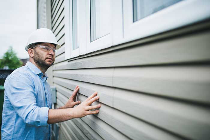 A professional from Wegner Roofing & Solar, wearing a hard hat and safety glasses, inspects newly installed vinyl siding on a house. The image focuses on the contractor, symbolizing quality assurance from expert Spearfish Siding Contractors.