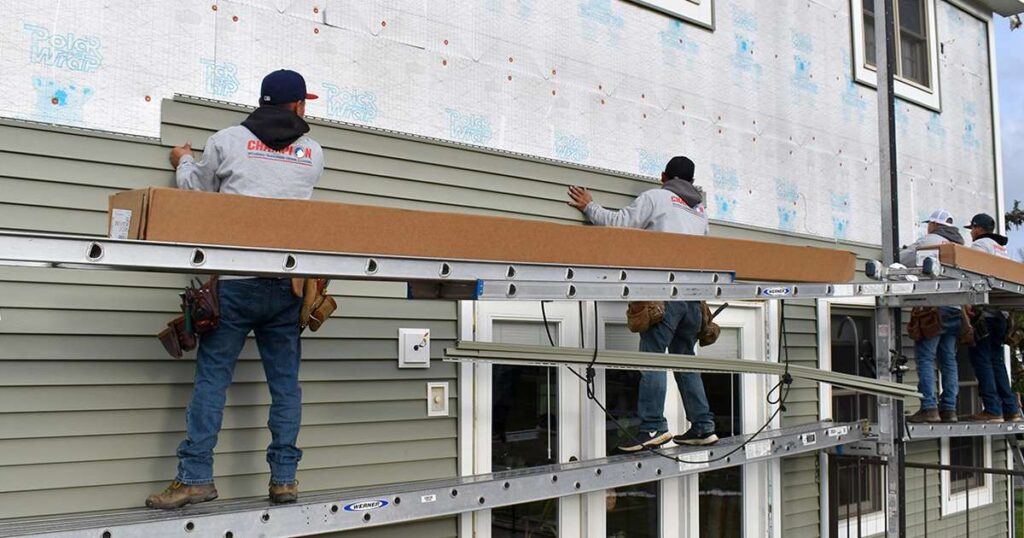 Spearfish Vinyl Siding Contractors from Wegner Roofing & Solar installing light green vinyl siding on the upper story of a residential home, using scaffolding to access the work area.