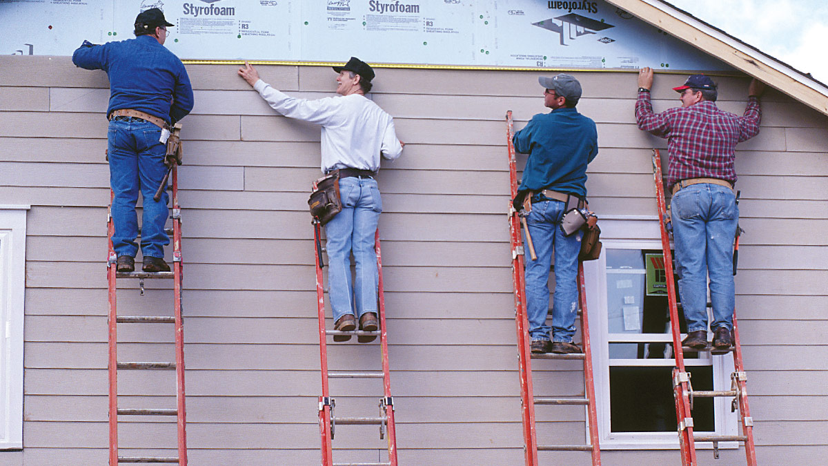 Four Spearfish Vinyl Siding Contractors from Wegner Roofing & Solar measuring and installing horizontal brown vinyl siding on a residential home while working on individual extension ladders.