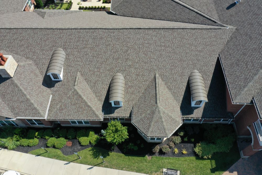 Aerial view of a complex roof featuring architectural shingles and custom metal barrel dormers installed by Carver MN Roofing Services.