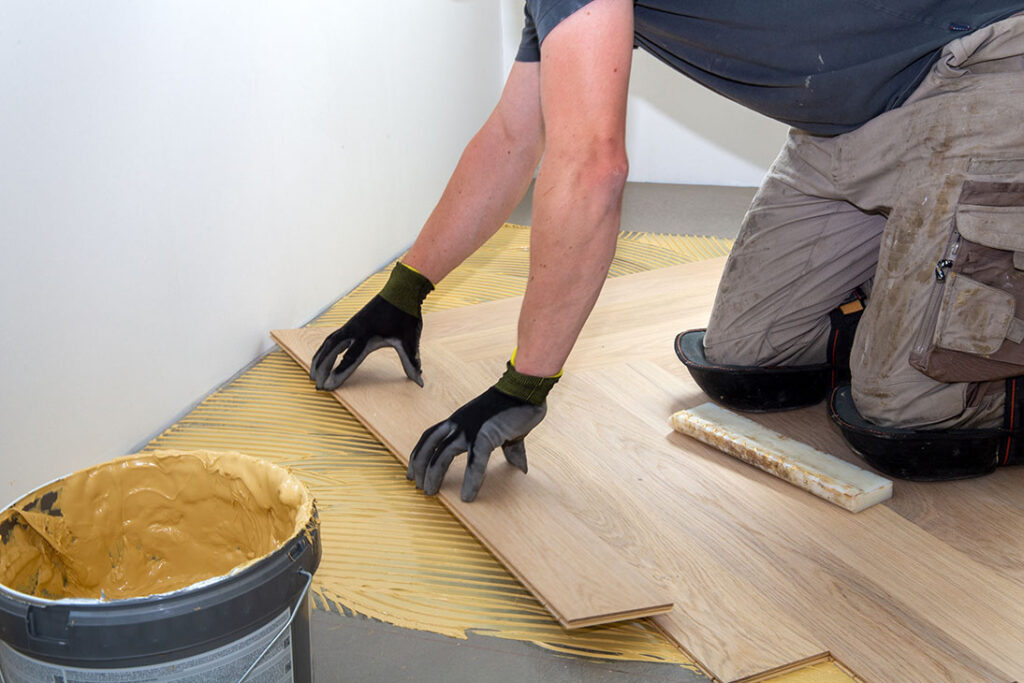 Commercial Flooring Installation Marietta GA by Peachy Flooring Solutions: Worker spreading adhesive and laying wood planks.