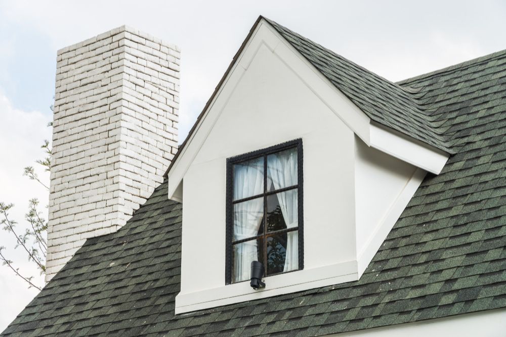 Close-up of a white dormer window and chimney after a professional Eugene residential roof repair.
