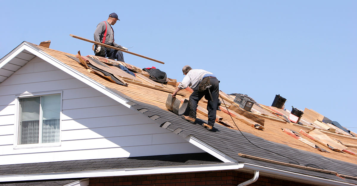 Two workers perform Residential Roofing Services Franklin NC by Burish Builders Asheville, removing old shingles from a house.