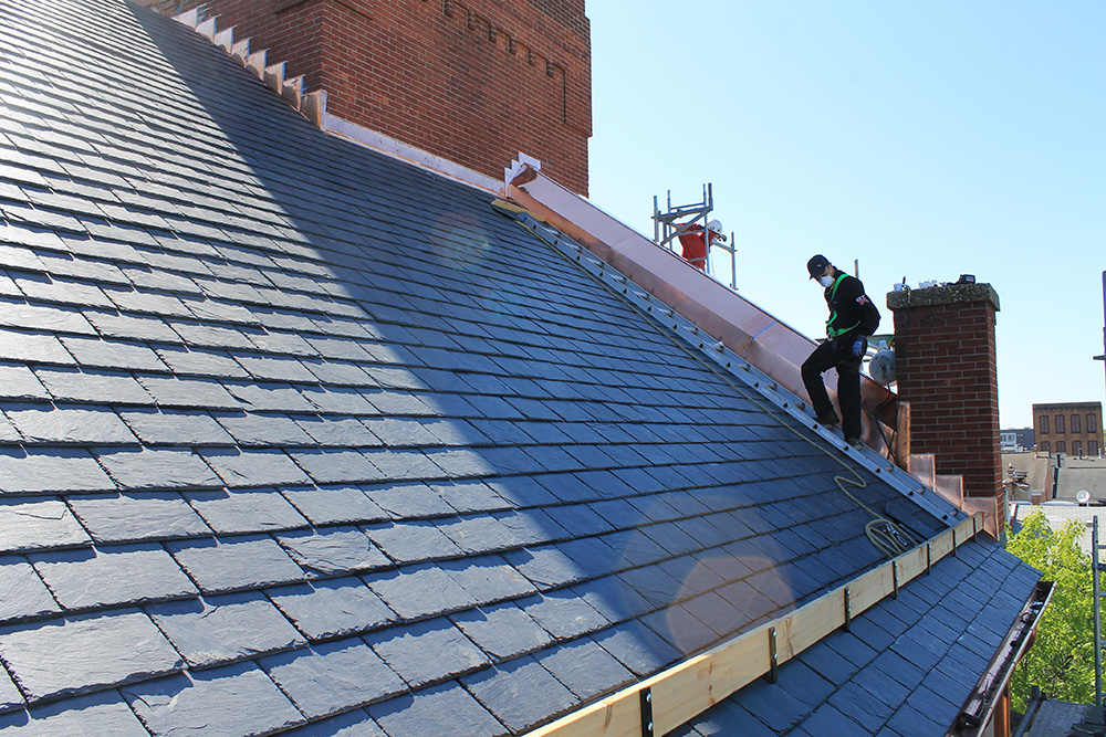 A professional from Roofing Company Hickory NC installing dark slate tiles on a steep roof with copper flashing.