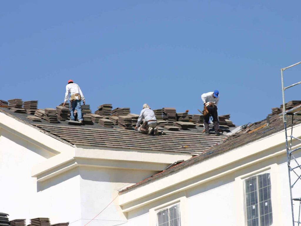Roofing Company Wrightsville Beach NC by Burish Builders Wilmington: Three workers install clay-colored roof tiles on a sunny day.