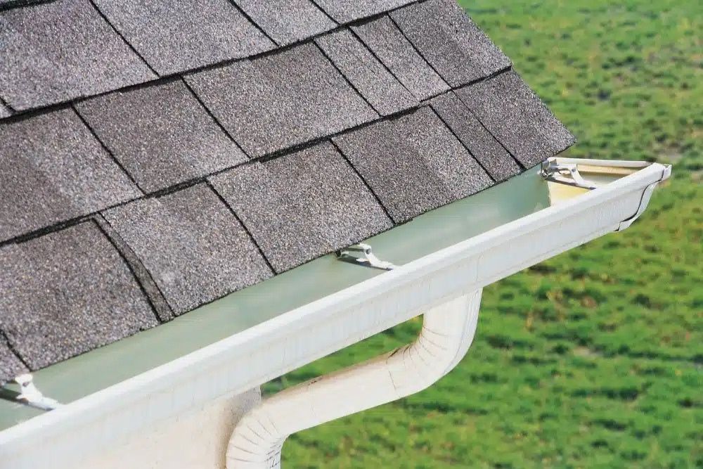 Close-up of residential roof shingles and white gutters requiring inspection for Anoka MN gutter damage.