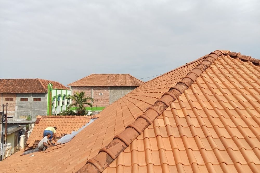 Professional contractors performing a Florence residential roof repair on a terracotta tile roof.