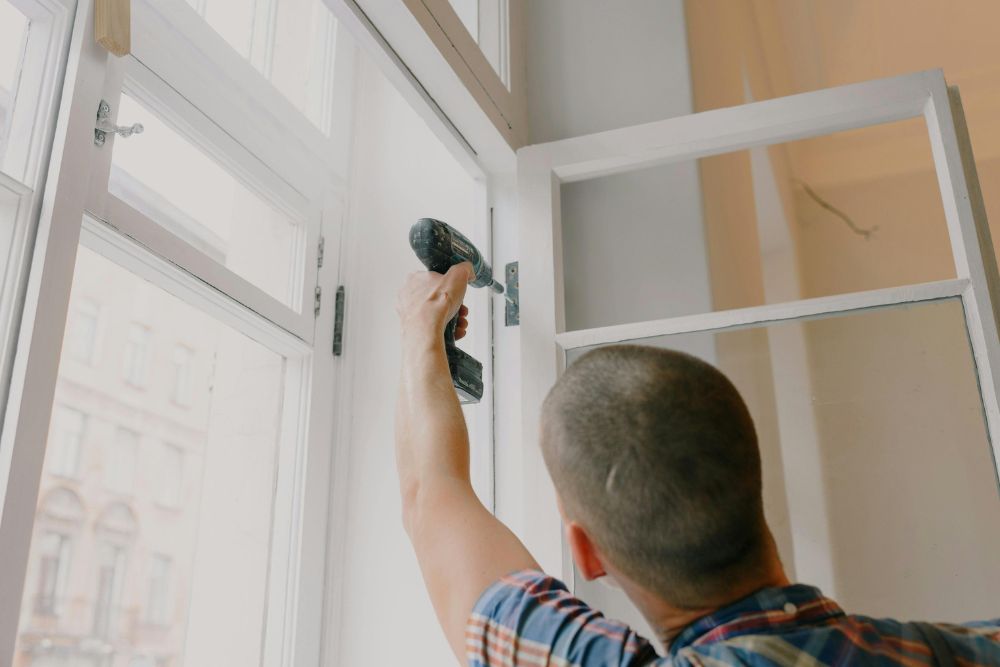 Professional Roseburg residential window installation technician securing a new white window frame with a power drill.
