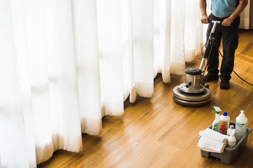 A professional technician performing a Summerfield hardwood clean and buff service using a floor rotary machine on light wood flooring.