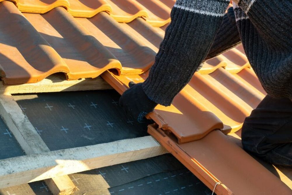 Close-up of a worker's hands during a Sutherlin residential roof repair, fitting a clay tile into place over protective underlayment.