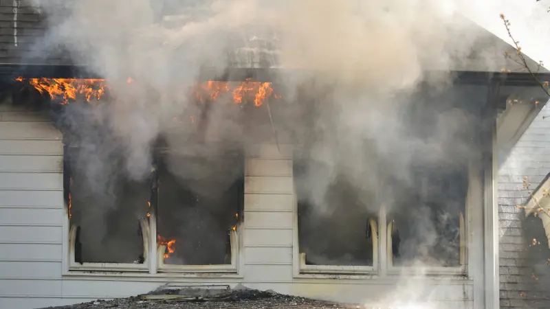 Fire Damage Repair Colorado Springs CO by Premier Carpet Cleaning: Smoke and flames engulfing a home's windows and roofline.