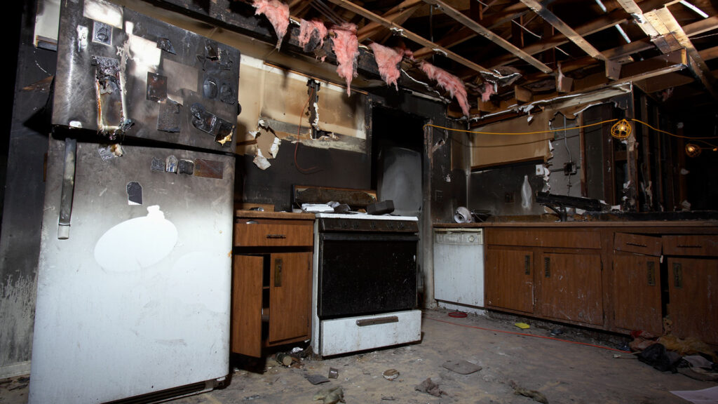 Fire Damage Restoration Colorado Springs CO by Premier Carpet Cleaning: Charred kitchen appliances and exposed ceiling beams.