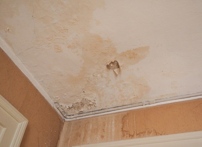 Water Damage Repairs Colorado Springs CO by Premier Carpet Cleaning: Close-up of yellow water stains and peeling ceiling paint.