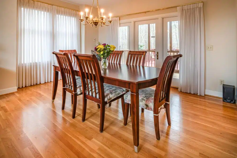 Professional hardwood floor refinishing Bellevue WA in a sunny dining room with a wooden table and chairs.