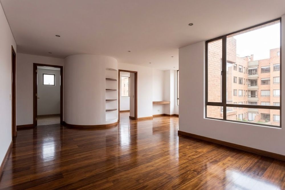 A wide-angle view of a professional hardwood floor refinishing Redmond WA project, showing glossy walnut floors framed by a modern architectural archway and natural window light.