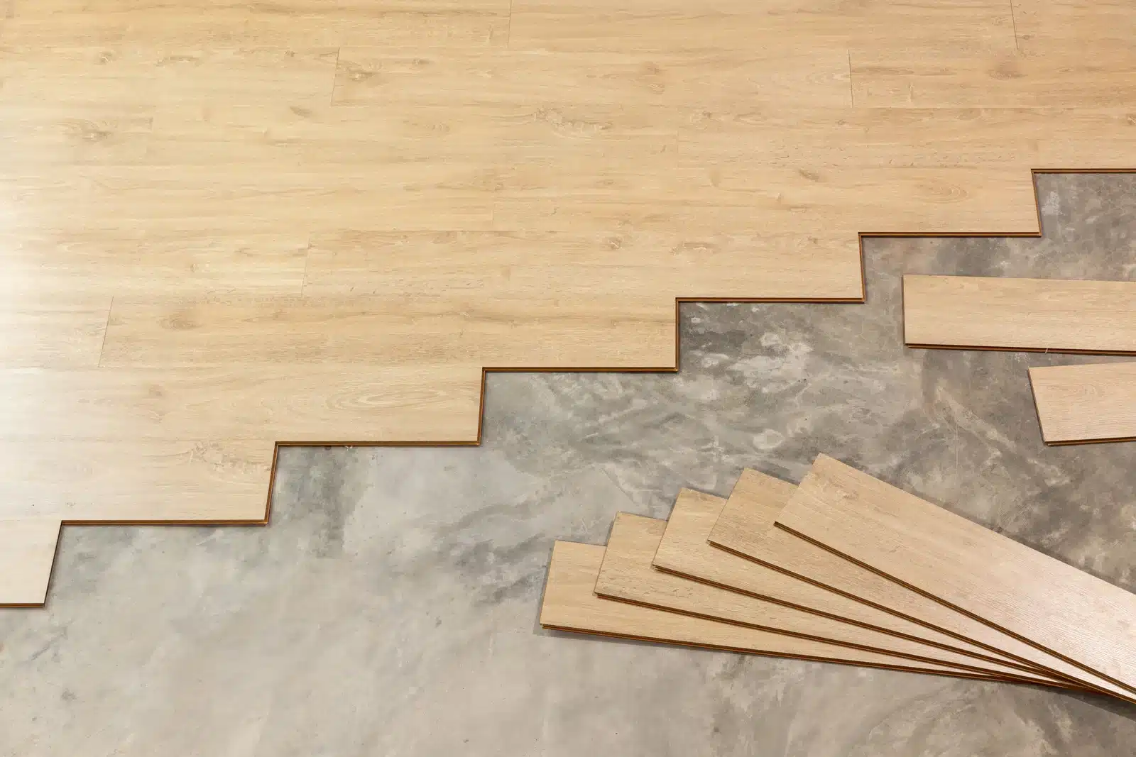 Hardwood Floor Installation Lenoir NC by Good House Floor Care shows light wood planks being laid over a concrete subfloor.