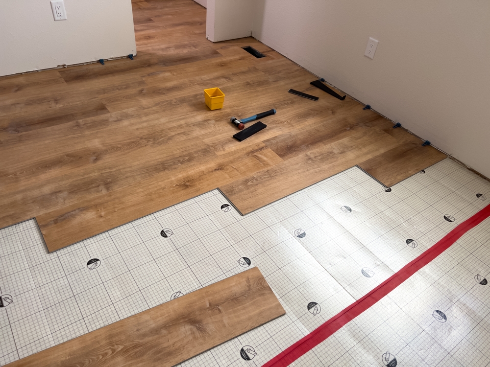Progress photo of a hardwood floor installation in Monroe, NC, by Good House Floor Care, with planks over underlayment and tools.